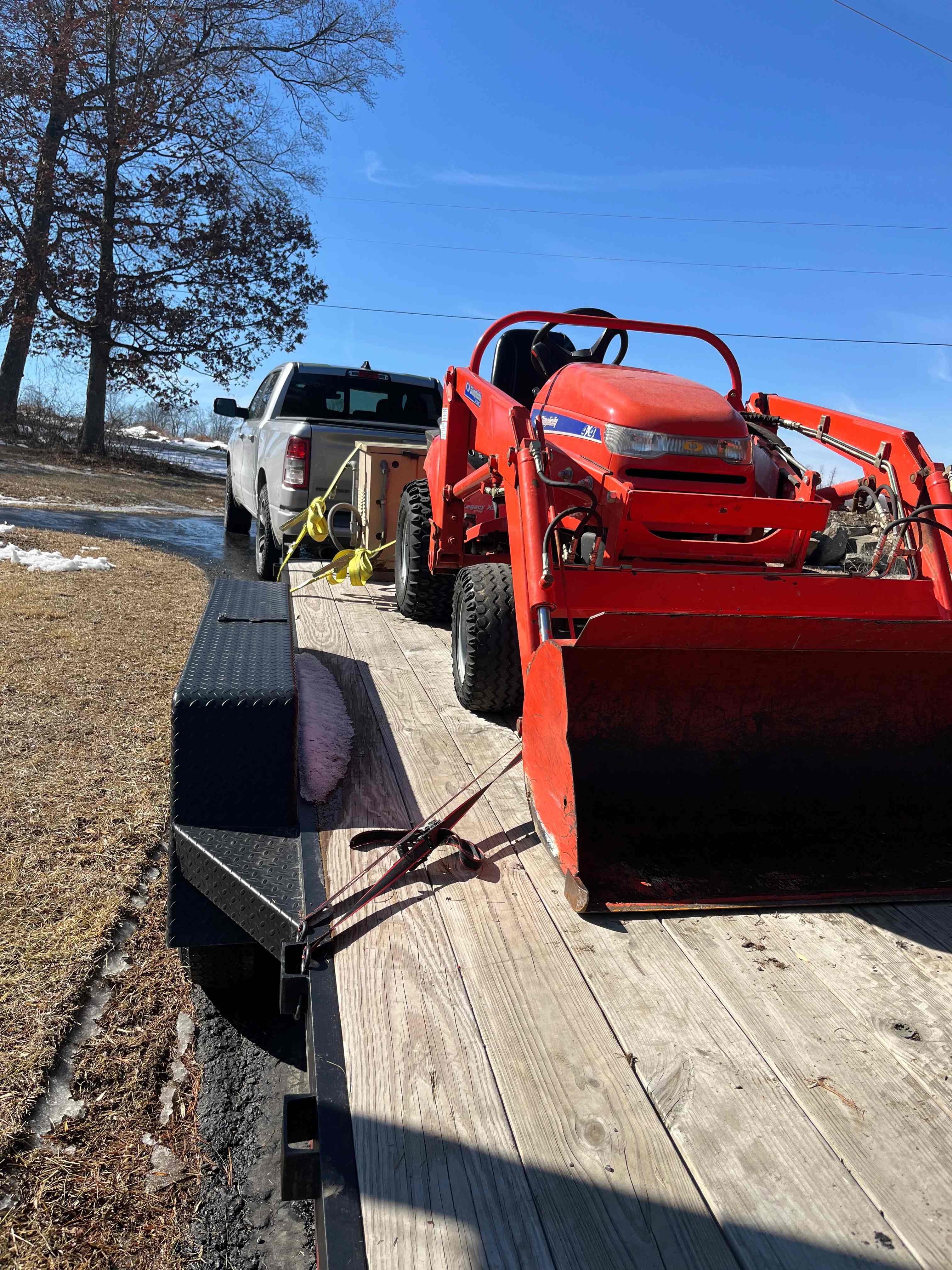Tractor with front loader being hauled on a flatbed trailer from Hawk Ridge Trailer Rentals
